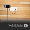 A black table lamp is plugged into a wall socket, with text overlay indicating charging features. Náhľad obrázku produktu