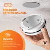 A hand holding a smoke detector mounting plate against a ceiling. Produktbild-Vorschau