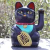 A black Maneki-neko cat figurine sits on a surface with a blurred green background. Produktbild-Vorschau