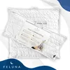 Two white quilted pillows are displayed, one partially covered by a clear plastic bag containing product information and an illustration of a person resting. The background is a gradient of white to light gray with abstract blue wave elements. Produktbild-Vorschau