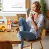 A woman is working on her laptop and drinking a smoothie at a wooden table. Voir les images du produit