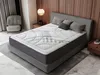 A bedroom scene with a mattress on a bed frame, pillows, a chair, and a nightstand. Produktbild-Vorschau