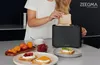 A woman is putting toast into a black toaster. There are fruits and prepared toast on the counter. Produktbild-Vorschau