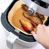 A hand is using red tongs to place sweet potatoes into an air fryer lined with parchment paper. Podgląd zdjęcia produktu