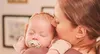 A mother holding her sleeping baby, who has a pacifier in their mouth. Produktbild-Vorschau