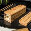 A close-up shot of a bamboo sushi-making tool with a sushi roll inside, placed on a black tray with chopsticks. Náhľad obrázku produktu