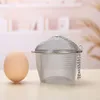 A tea infuser and an egg are placed on a wooden surface with a blurred background of shelves and plants. Produktbild-Vorschau