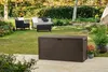 A brown storage box is placed on a patio in a backyard setting, with outdoor furniture and greenery in the background. Podgląd zdjęcia produktu