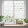 A close-up view of two white roller blinds with a wave pattern, covering a window with a view of greenery outside. On the windowsill below, there is a vintage radio, a decorative sheep figurine, and a potted plant. Produktbild-Vorschau