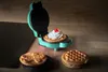 A teal mini waffle maker on a wooden surface with waffles. Podgląd zdjęcia produktu