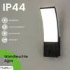 A black outdoor wall light with a curved white light panel is mounted on a textured gray wall. Text and icons detailing the product's features are on the left side of the image. Anteprima dell’immagine prodotto