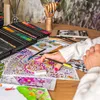 A person's hands are coloring in a detailed adult coloring book with a set of colored pencils. Produktbild-Vorschau