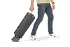 A person is pulling a folded travel cot with wheels. Náhled obrázku produktu