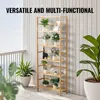 A multi-shelf wooden plant stand filled with various potted plants, displayed on a balcony with a white slatted wall and railing in the background. Anteprima dell’immagine prodotto
