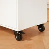 Close-up of the bottom of a white cabinet with black casters on a wooden floor. Produktbild-Vorschau