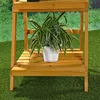 A wooden plant stand with a potted plant on one of its shelves, set against a green grassy background. Produktbild-Vorschau