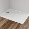 A white rectangular shower tray with a silver drain is shown in a corner against a light gray wall, with a wooden floor in the foreground. Produktbild-Vorschau
