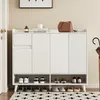 A white shoe cabinet with a drawer and four doors, placed in an entryway with shoes on the shelves and a rug on the floor. Produktbild-Vorschau