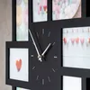 A close-up view of a black photo frame wall clock with white clock hands and markings. Several small framed pictures are visible around the clock face, some containing colorful abstract images and others featuring heart designs. Produktbild-Vorschau