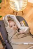 A baby wrapped in a blanket in a car seat, with a lamp in the background. Produktbild-Vorschau