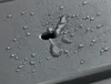 A close-up of water droplets on a textured gray surface with a hole. Produktbild-Vorschau