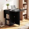 A black folding table with shelves and a drawer, set up in a room next to a bookshelf. A laptop, vase with flowers, and a coffee cup are on the table. Náhľad obrázku produktu