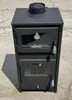 A black wood-burning stove with a chimney pipe on top, placed outdoors on a concrete surface. Produktbild-Vorschau