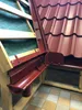 A close-up view of a red metal roof tile and gutter system, showcasing construction materials. Produktbild-Vorschau