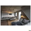 A modern living room with concrete walls and ceiling, featuring a sectional sofa, a floor lamp, and a table lamp. Produktbild-Vorschau