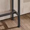 A close-up view of the black metal legs and adjustable feet of a console table, resting on a wooden floor against a textured wall. Podgląd zdjęcia produktu