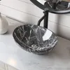 A close-up shot of a black and white marble-patterned vessel sink with a black faucet, placed on a white marble countertop. Produktbild-Vorschau