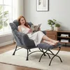 A woman is reading a magazine while sitting in a comfortable armchair with a footrest. Produktbild-Vorschau