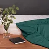 A green fitted sheet is draped over a mattress, with a vase of flowers and a notebook on a wooden surface in the foreground. Anteprima dell’immagine prodotto