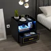 A black nightstand with gold accents and LED lighting is placed next to a bed in a bedroom. Náhled obrázku produktu