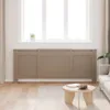 A radiator cover is placed in front of a window in a living room, with a coffee table and sofa visible. Náhled obrázku produktu