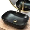 A black oval basin with gold fixtures sits on a wooden surface, with a gold-rimmed mirror reflecting the scene. Náhľad obrázku produktu
