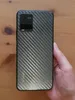 A hand holding a smartphone with a carbon fiber pattern on the back. Produktbild-Vorschau