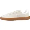 A side view of a single beige Lacoste sneaker with a white heel accent and a brown sole, set against a white background. Produktbild-Vorschau