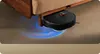 A black robot vacuum cleaner is cleaning the floor under a wooden sofa. Voir les images du produit