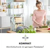 A woman is preparing food in a kitchen next to a mini-fridge. Produktbild-Vorschau