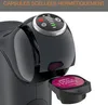 A close-up of a black coffee machine with a pink coffee capsule being inserted. Voir les images du produit
