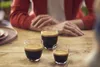 Three glasses of espresso on a wooden table with a person in the background. Anteprima dell’immagine prodotto