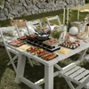 A picnic table set up outdoors with a raclette grill, food, and chairs. Náhľad obrázku produktu