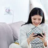 A woman is sitting on a couch, holding a phone that is plugged into a wall charger. Anteprima dell’immagine prodotto