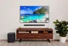 A living room setup with a TV, soundbar, subwoofer, and entertainment center. Produktbild-Vorschau