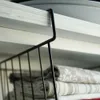 A close-up view of a black metal hanging basket hooked onto a shelf, with folded blankets inside. Anteprima dell’immagine prodotto