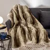 A plush throw blanket draped over a sofa, with a side table holding a mug and a lamp. Náhled obrázku produktu