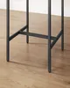 The base of a black table is shown on a light wood floor, with a white wall in the background. Produktbild-Vorschau