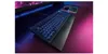 A gaming keyboard with blue backlighting on a desk with purple lighting. Produktbild-Vorschau