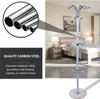 A white coat rack with multiple hooks stands in a bedroom setting next to a bed and nightstand. A close-up inset shows the material of the coat rack. Náhled obrázku produktu